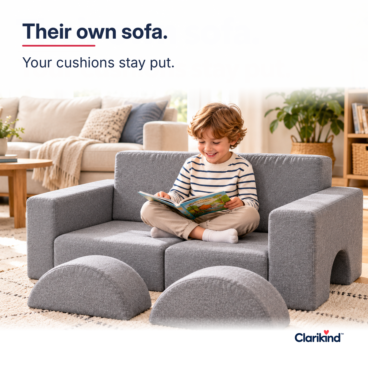 Child reading a picture book on the grey modular play sofa in a bright family living room