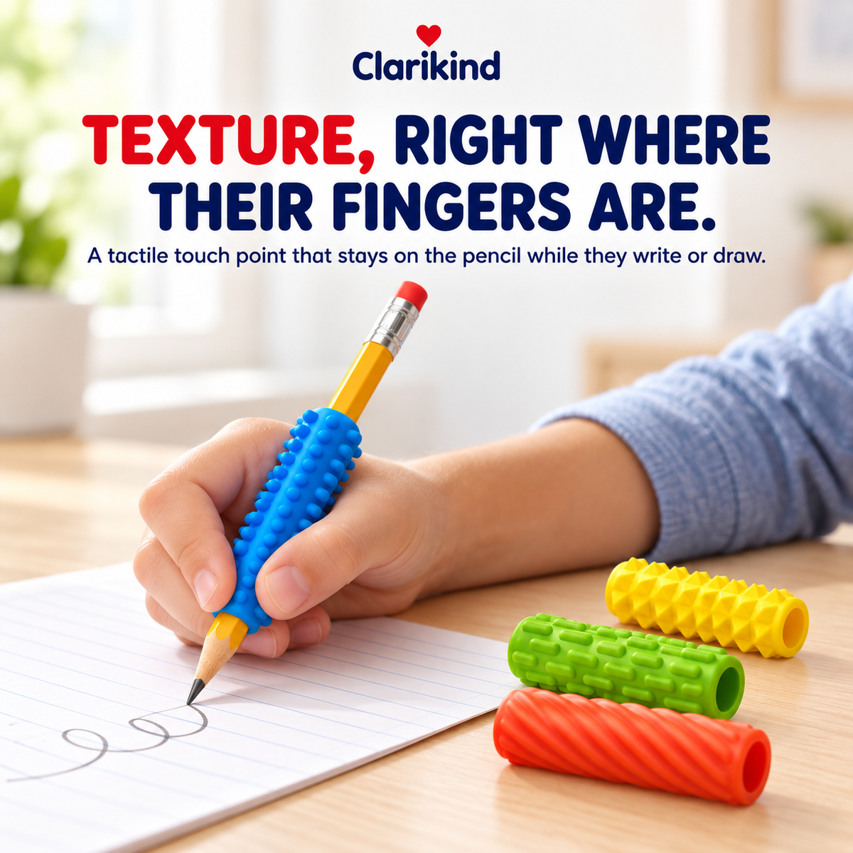 Child writing with a blue textured pencil grip, other grips beside the page