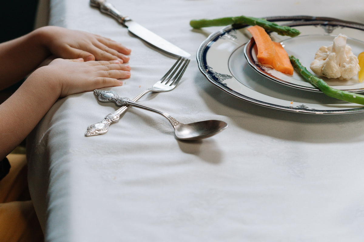Child's hands beside a plate of vegetables at a family meal